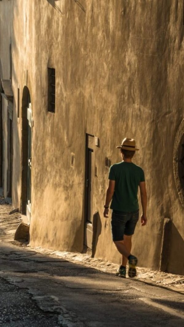 Ein einsamer junger Mann, der die Straße entlang neben einem alten Betongebäude geht.